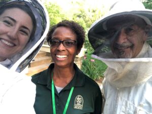 A group of people smiling, wearing beekeeper suits.